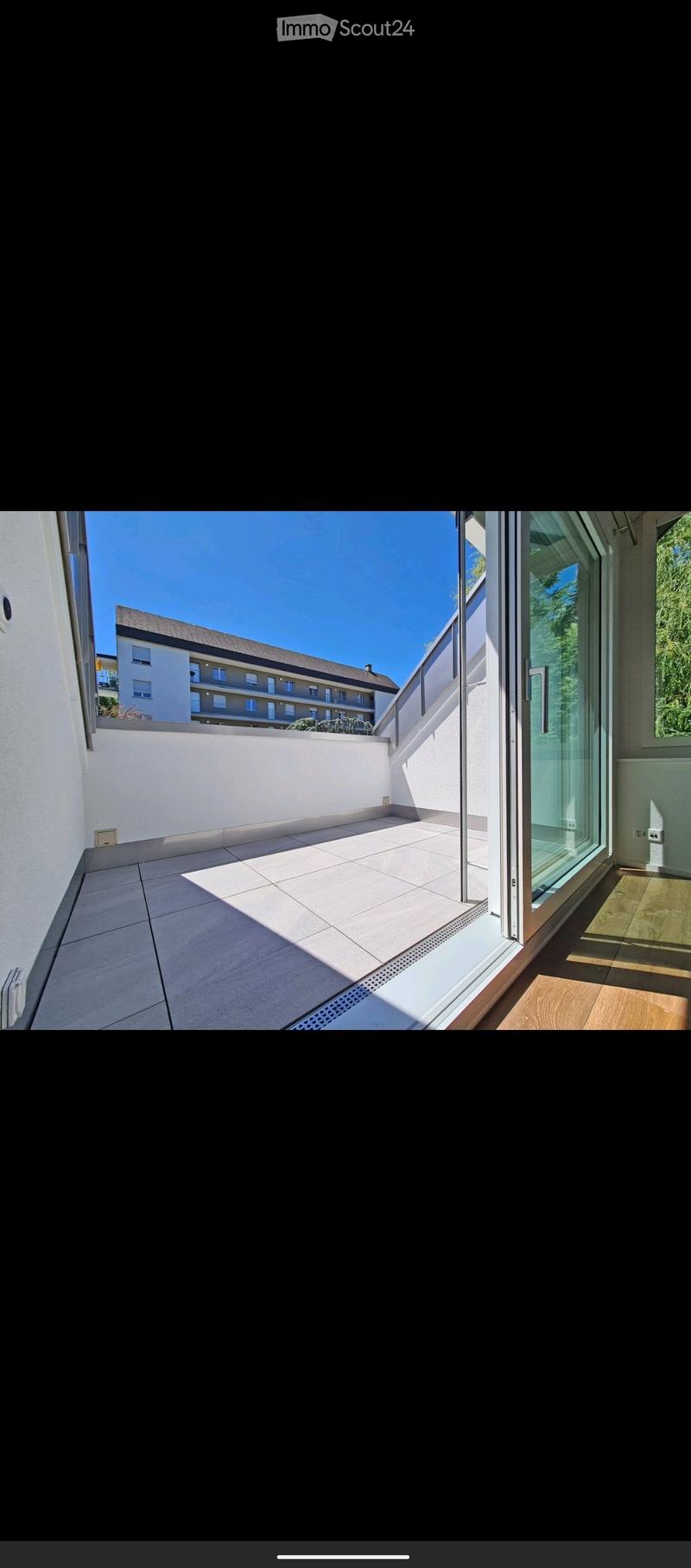 Balcony with tiled floor, white walls, and a view of a building and greenery.
