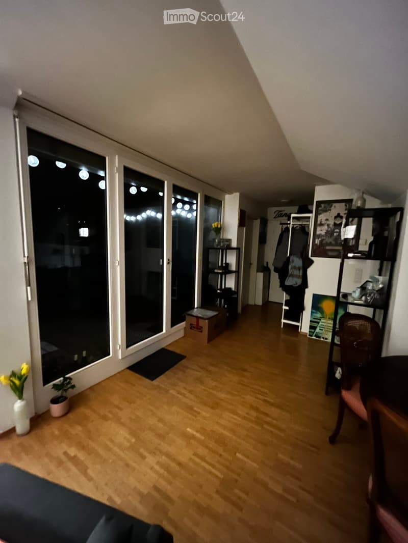 A furnished room with wooden flooring, large windows, a chair, shelves, and decorative vases.