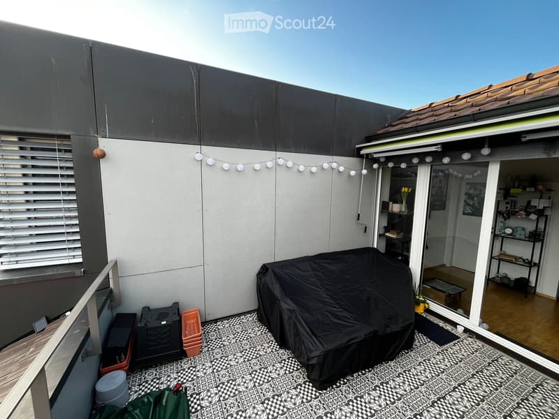 Balcony with patterned tile flooring, covered grill, and string lights, connected to an indoor space with shelves and decor.