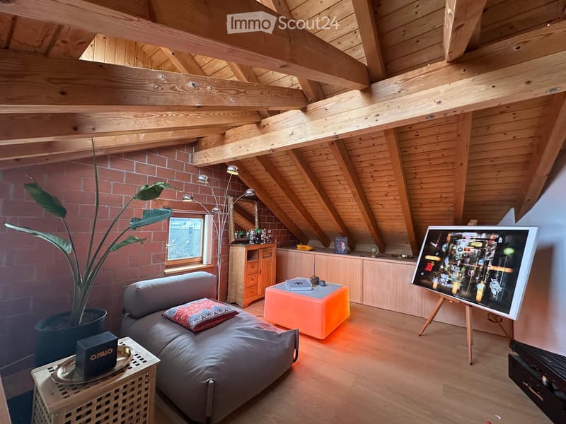 Loft-style living room with wooden beams, exposed brick wall, large window, sofa, coffee table, floor lamp, cabinet, and artwork on an easel.
