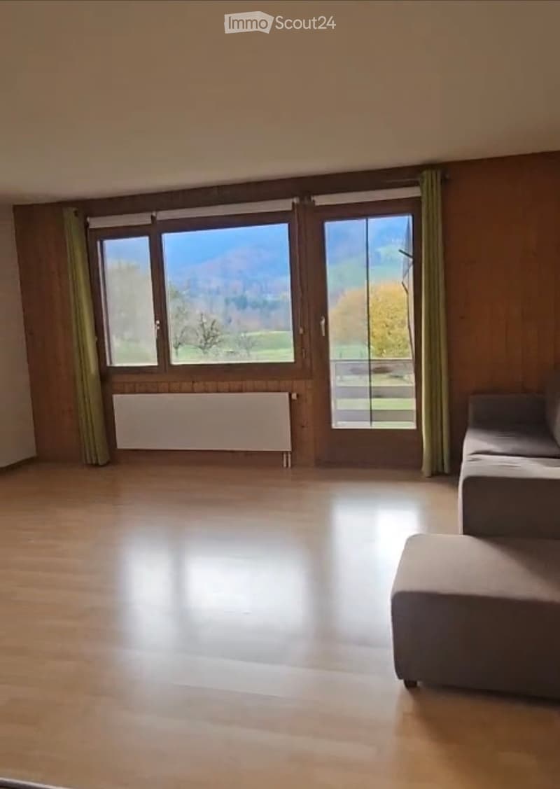 Spacious room with wooden flooring, large windows offering a scenic view, and a single sofa in the corner.