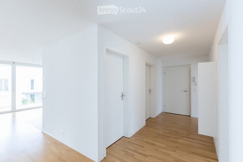 Empty hallway with white walls, wooden flooring, and a large sliding glass door leading to a balcony.