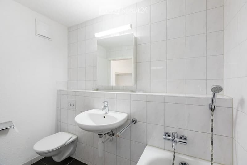 Modern bathroom with white tiles, a sink, toilet, bathtub, and a large mirror above the sink.