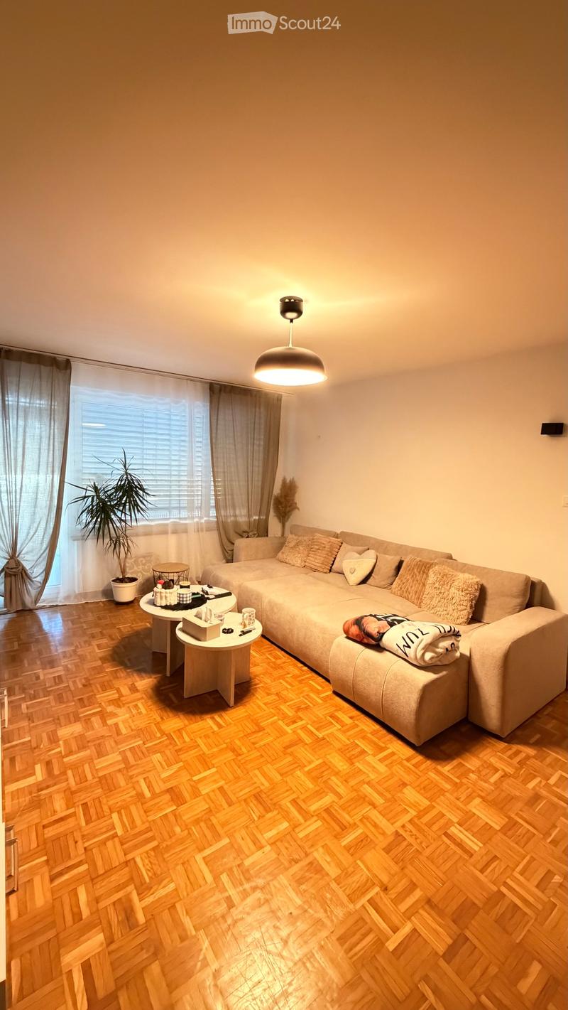 Modern living room with a large sectional sofa, wooden herringbone flooring, pendant light fixture, and small side tables.