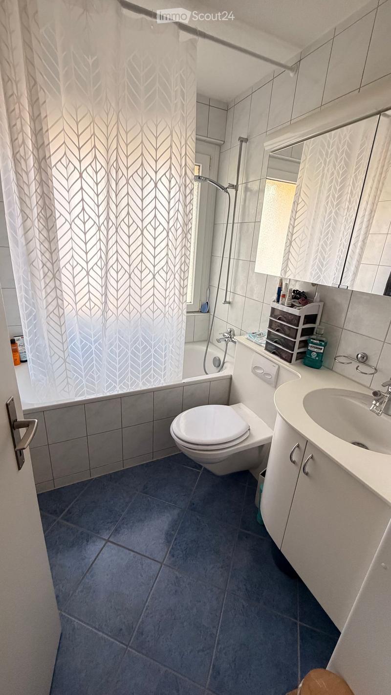 Modern bathroom with blue tiles, white fixtures, a toilet, sink, bathtub, and a shower area with a curtain.