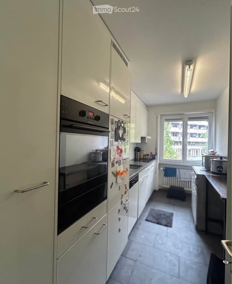 Modern kitchen with white cabinets, stainless steel appliances, and a large window offering a view of the city.