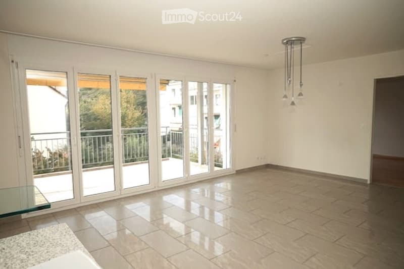 Empty room with large sliding glass doors leading to a balcony, tiled floor, and a glass side table near the entrance.