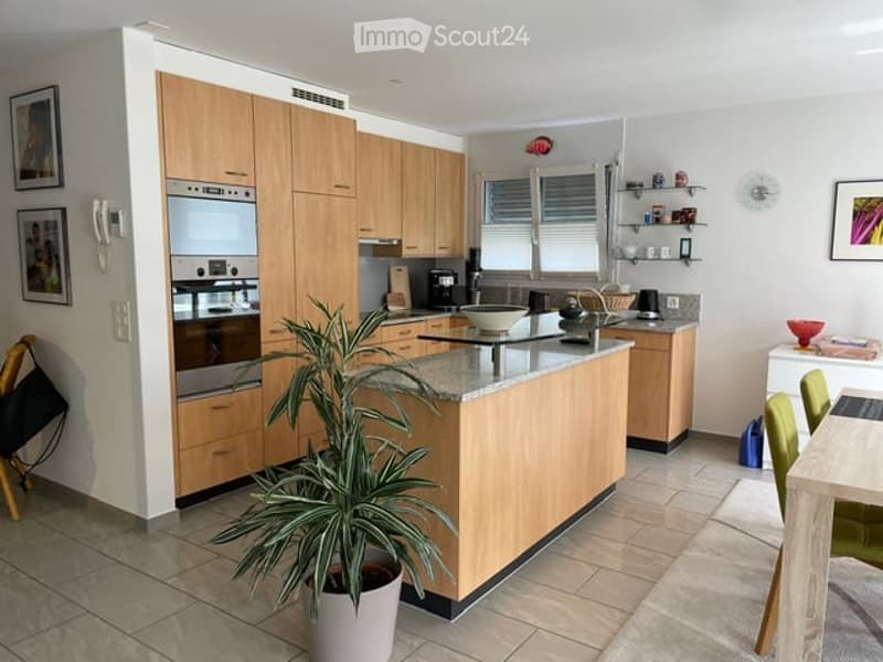 Modern kitchen with light wood cabinetry, stainless steel appliances, granite countertop, and a small dining area with chairs and a table.