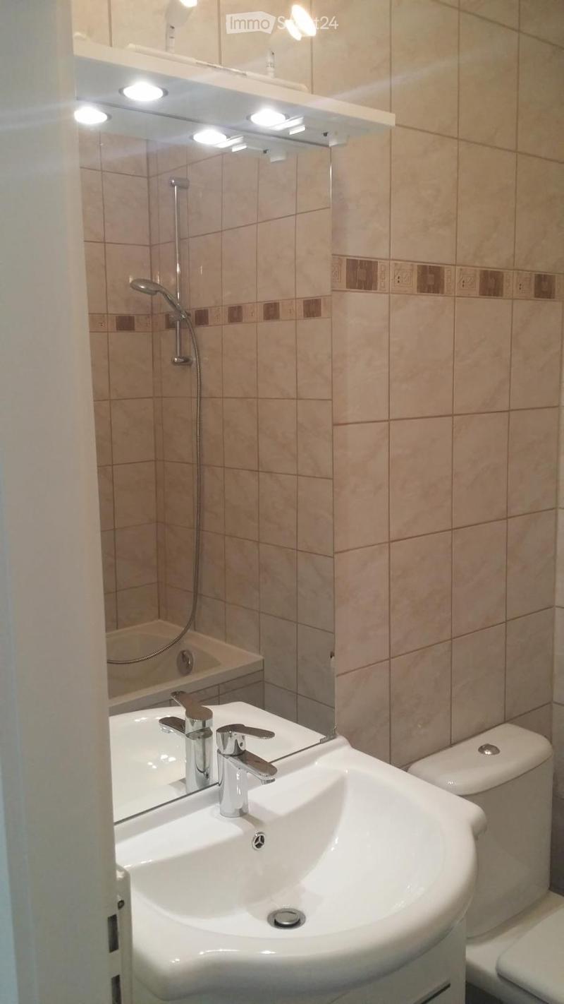 Modern bathroom with a white sink, chrome faucet, large mirror with built-in lighting, and a shower area with a handheld showerhead.