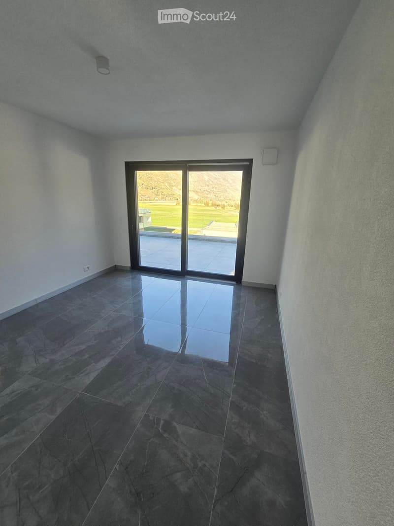 Empty room with dark tiled floor, white walls, and large sliding glass door leading to outdoor area with pool and landscape.