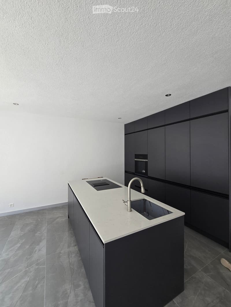 Modern kitchen with white countertop, black cabinets, and a stainless steel sink and faucet.