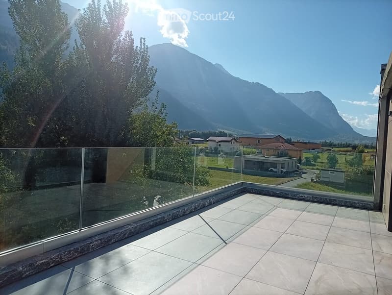 A modern balcony with a glass railing, tiled floor, and scenic mountain view.