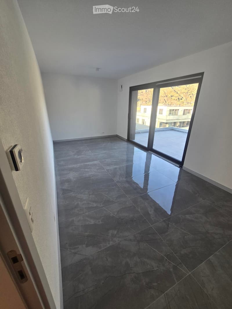 Empty room with dark grey tiled floor, white walls, and large sliding glass door leading to a balcony.
