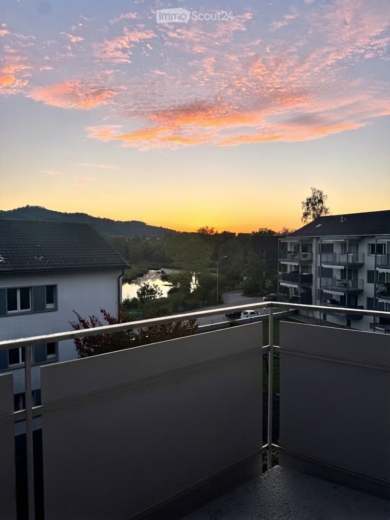 Balcony overlooking a scenic view of a river, surrounding buildings, and a sunset sky.