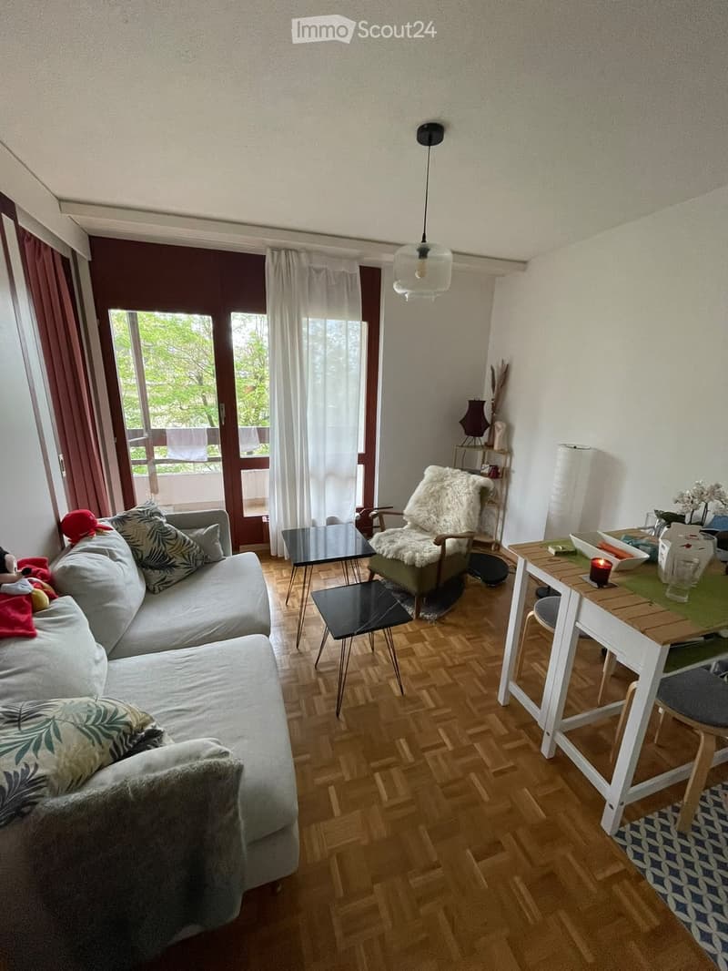 A modern living room with a grey sofa, wooden floor, a small table, and a balcony view.