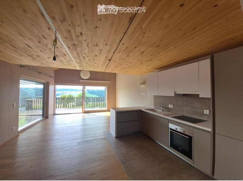 Modern kitchen with light wood flooring, white cabinets, stainless steel appliances, and large windows offering a scenic view.