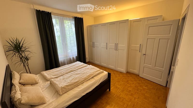 Cozy bedroom with a double bed, white wardrobe, and a potted plant near the window.