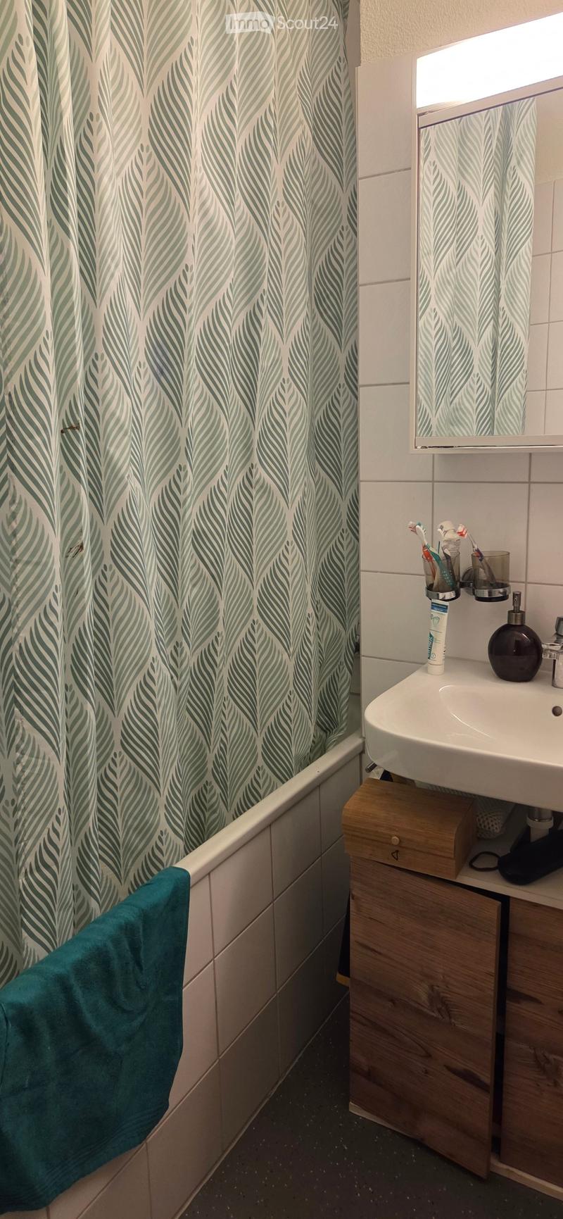 Bathroom with a bathtub, shower curtain, sink, mirror, toothbrush holder, soap dispenser, and a towel draped over the edge of the tub.
