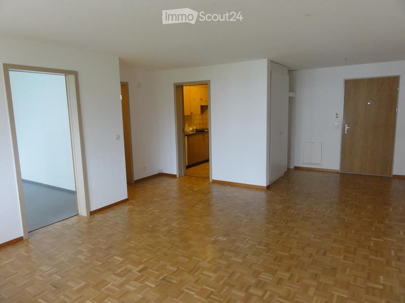 Empty room with wooden flooring, white walls, and several doors leading to other rooms.