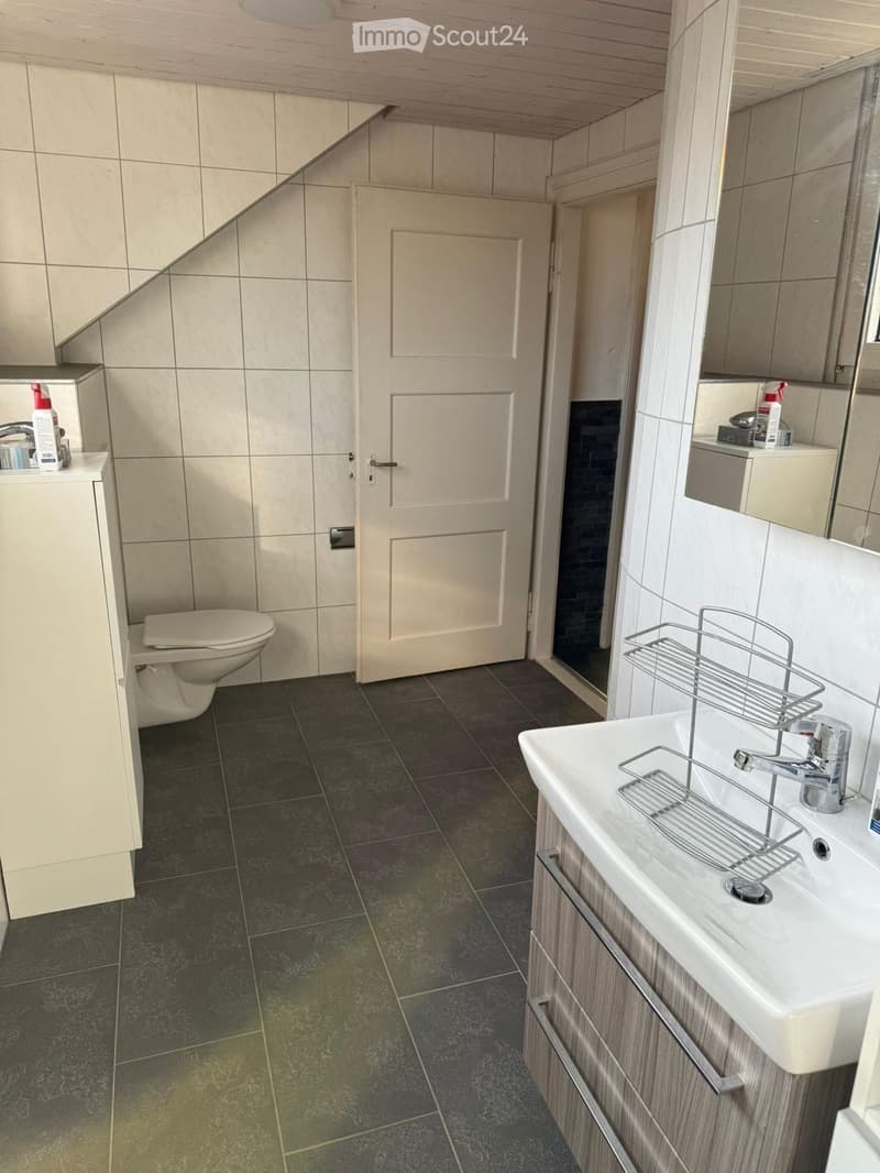 Modern bathroom with dark tiled floor, white sink with chrome faucet, toilet, mirrored cabinet, and a door leading to another room.