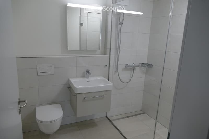 Modern bathroom with white tiles, a sink with a mirror, a toilet, and a glass-enclosed shower area.