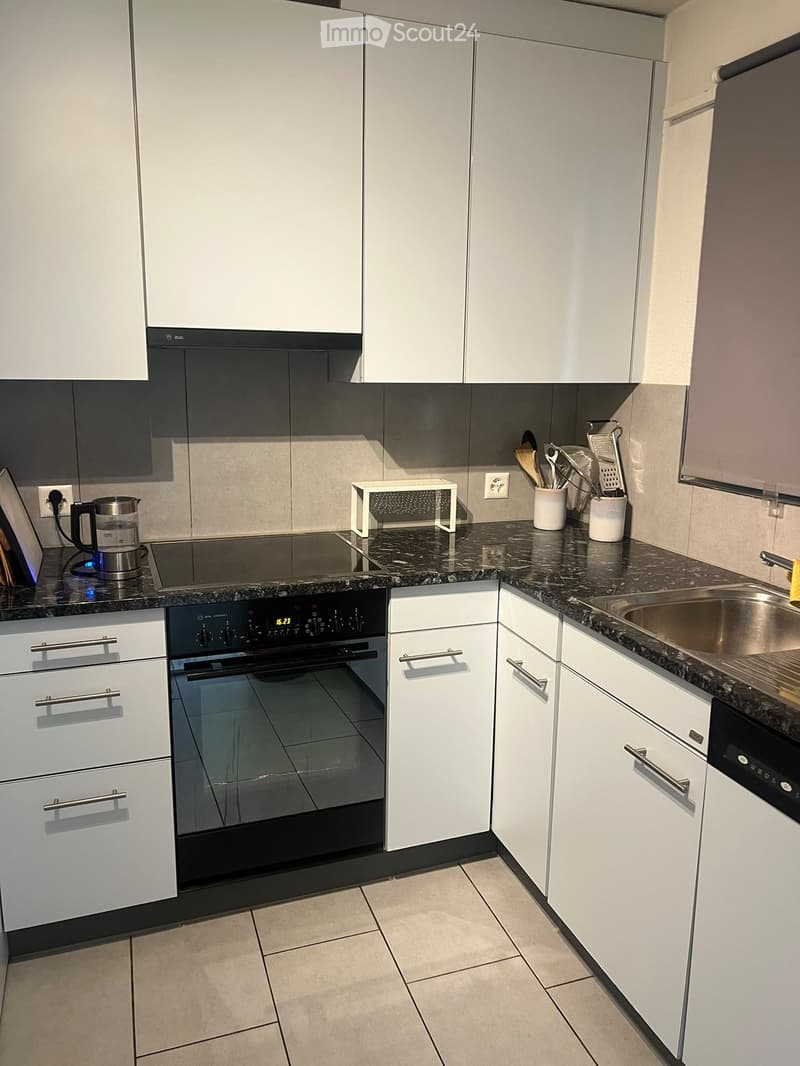 Modern kitchen with white cabinets, granite countertops, stainless steel sink, built-in oven, and various appliances and utensils.