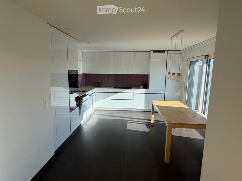 Modern kitchen with white cabinets, black tiled floor, and a wooden dining table near a large window.