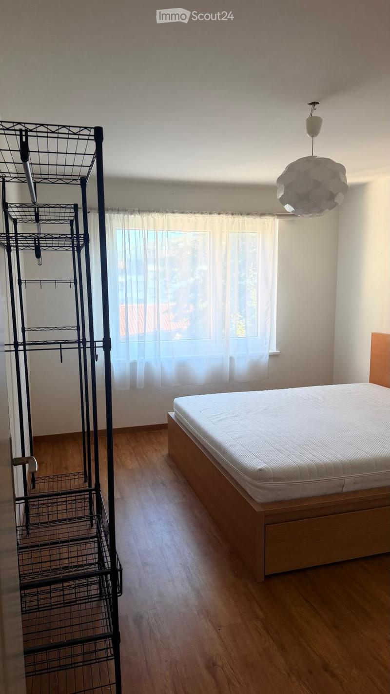 A tidy bedroom with a wooden bed frame, a mattress, a hanging rack, and a modern pendant light fixture.