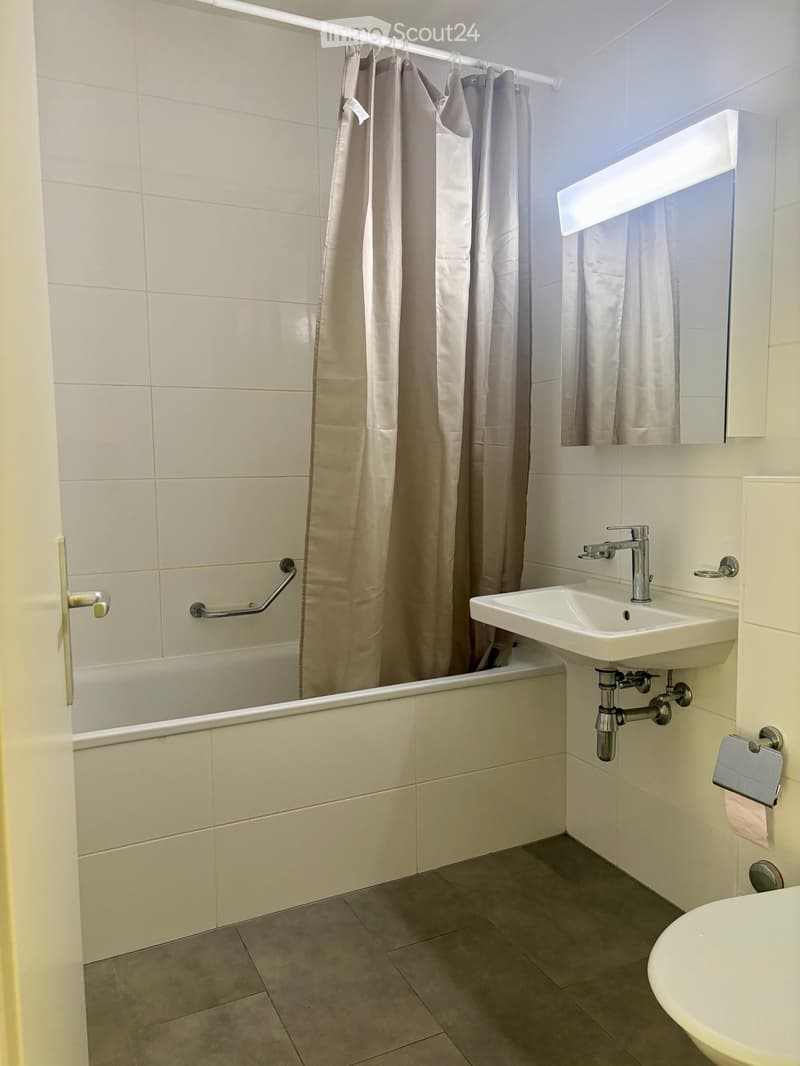 Modern bathroom with a bathtub, sink, mirror, and shower curtain. Features a chrome faucet and a towel rack.