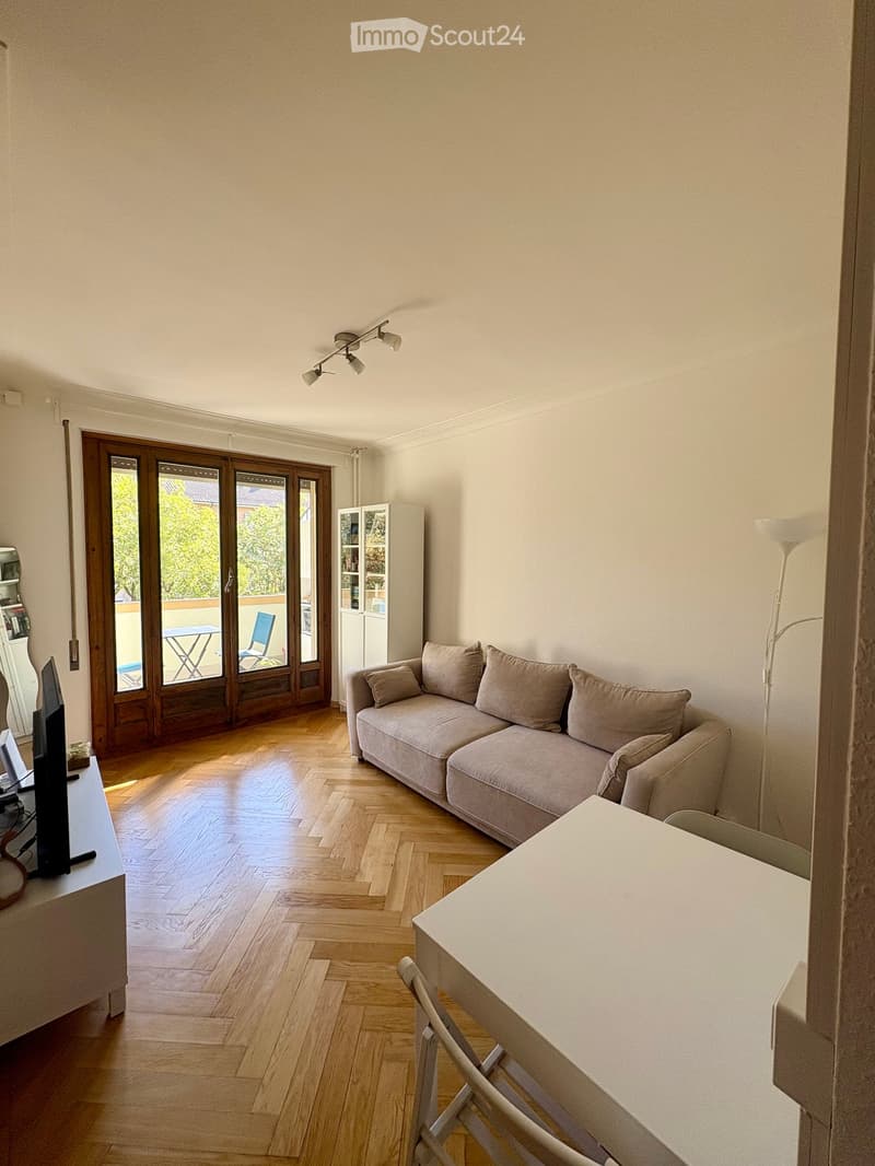 Living room with wooden floor, sofa, table, chairs, screen, cabinet, and lamp. Large sliding doors lead to a balcony.