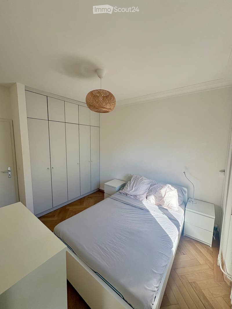 Modern bedroom with a neatly made bed, white nightstands, built-in wardrobes, and a hanging woven lamp.