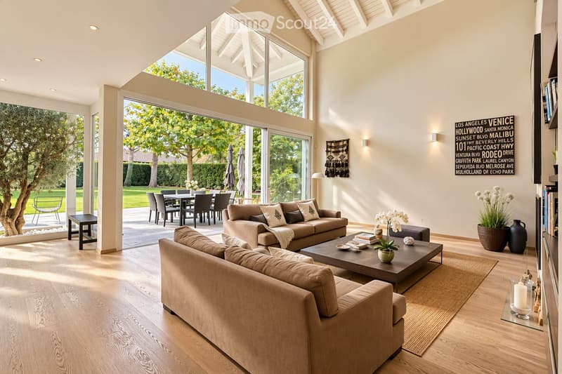 Modern living room with large windows, two sofas, coffee table, ottoman, dining area with table and chairs, and decorative vases.