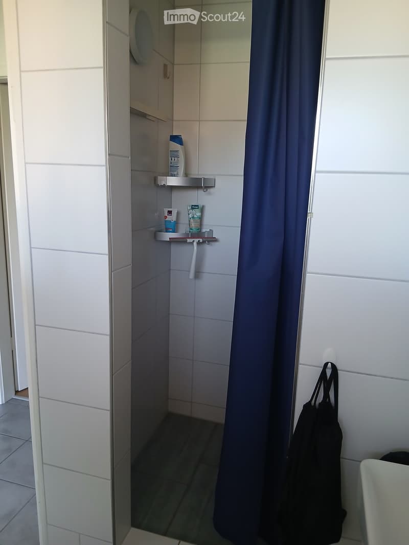 Shower area with white tiled walls, a blue shower curtain, a small shelf holding toiletries, and a towel hanging on the side.