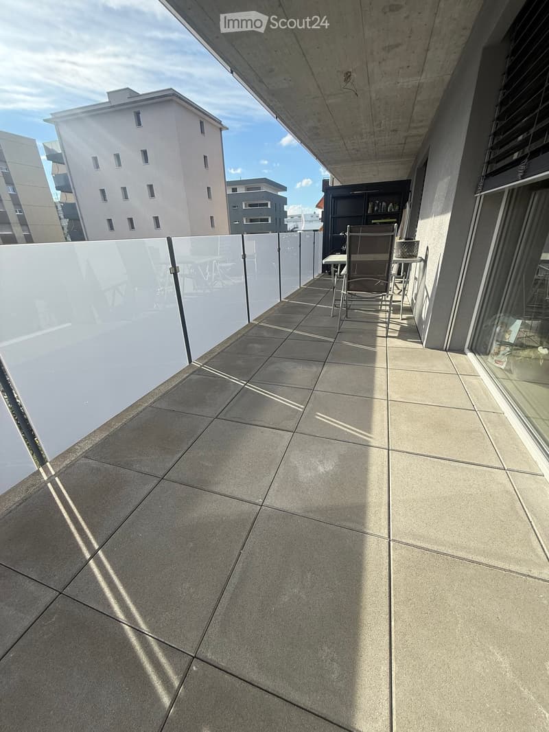 Balcony with tiled floor, glass railing, and a small table and chair set.