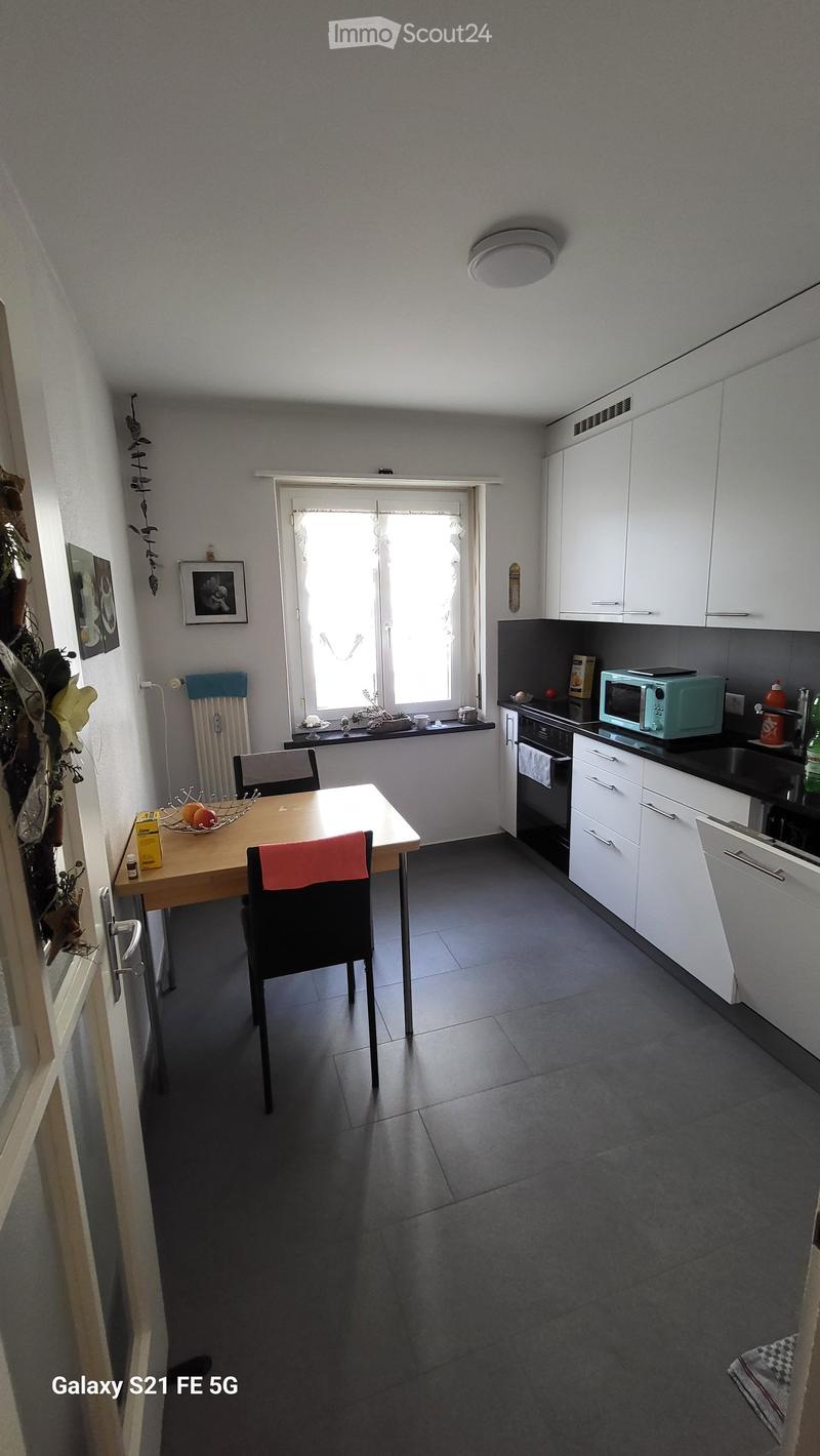 Modern kitchen with white cabinets, black countertops, a wooden dining table with chairs, a microwave, and a fruit bowl on the table.