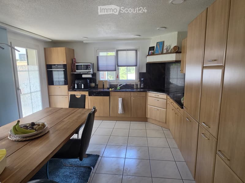 Bright kitchen with light wooden cabinets, a dining table with chairs, and various appliances including a microwave, coffee maker, and dishwasher.