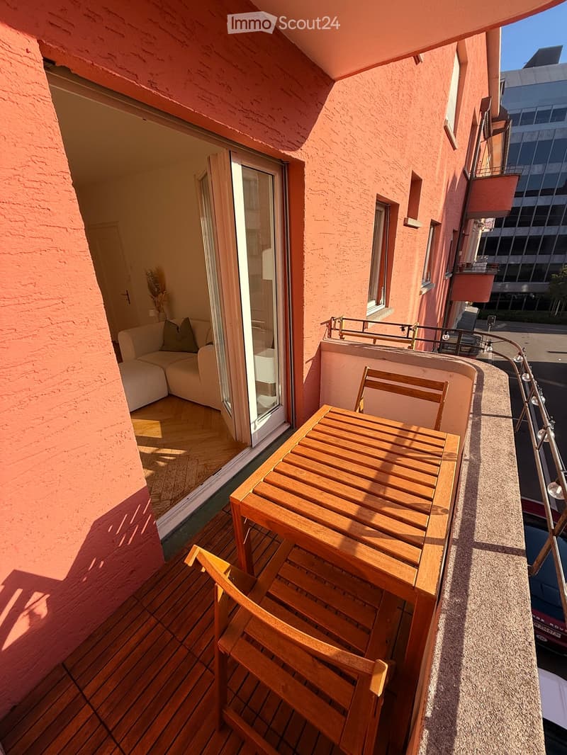 Balcony with wooden table and chairs, overlooking a cityscape with modern buildings.