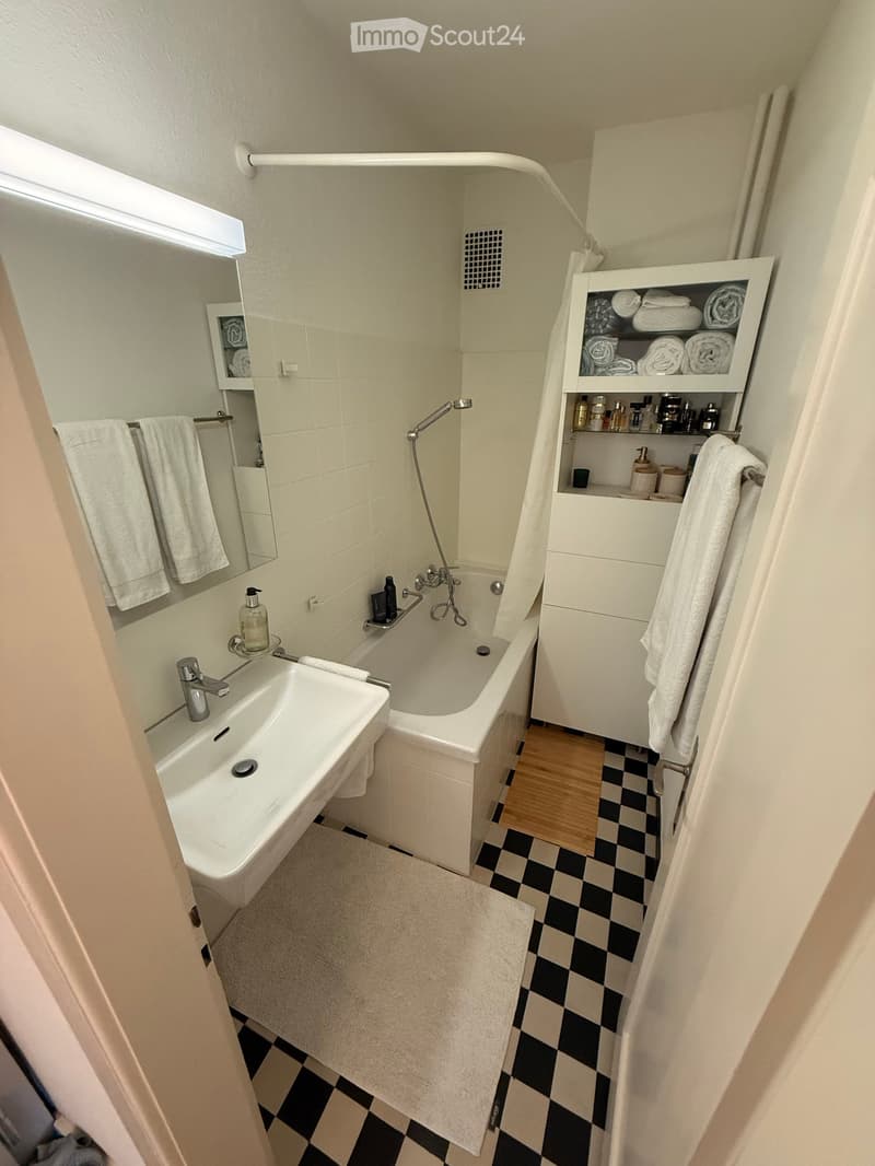 Modern bathroom with a bathtub, sink, mirror, towel rack, and a white cabinet with shelves holding towels and toiletries.