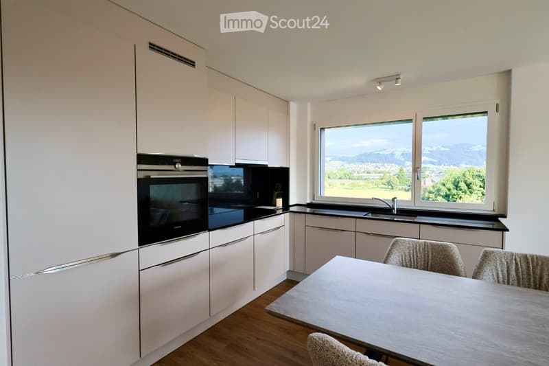 Modern kitchen with white cabinets, black countertops, integrated oven, and large windows offering a scenic view.