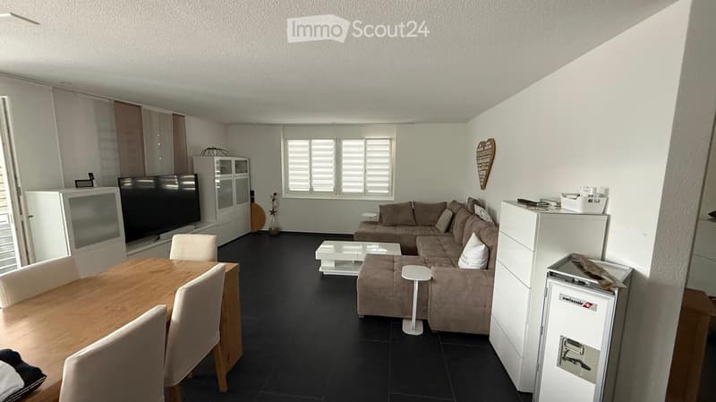 Modern living room with a sectional sofa, coffee table, dining table with chairs, TV, and white cabinets.