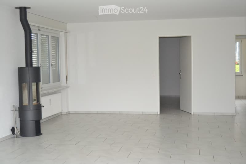 Empty room with light-colored tiled flooring, white walls, and a modern black wood-burning stove with a chimney. There is a doorway leading to another room.