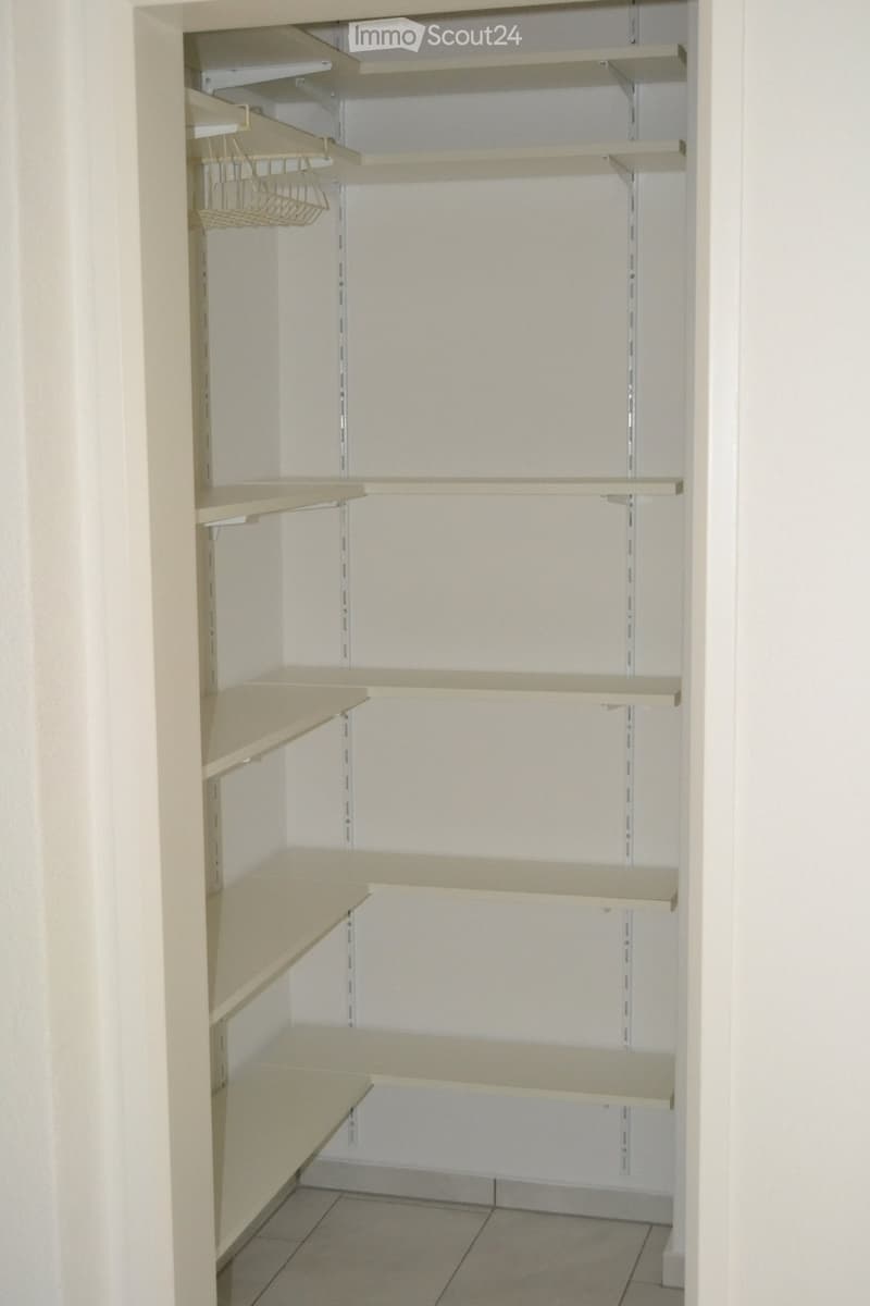 Empty closet with multiple beige shelves and a small wire basket on the top left shelf.