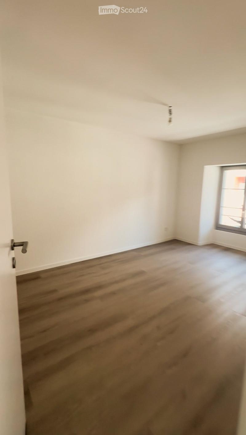 Empty room with wooden flooring and white walls, featuring a single window and a door.
