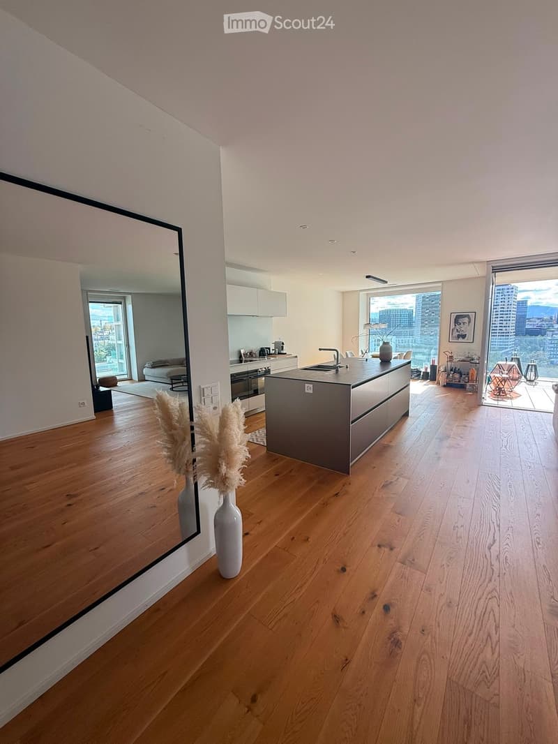 Open-concept kitchen and living area with wooden flooring, modern kitchen island, large windows offering city views, and decorative vases.