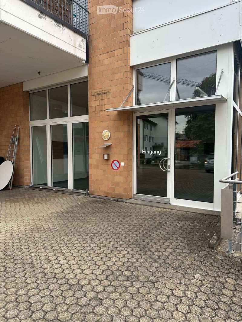 Entrance area of a building with glass doors, brick walls, and a paved ground.