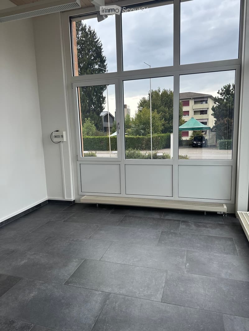 Empty room with large windows, grey tiled floor, white walls, radiator, and electrical outlet.