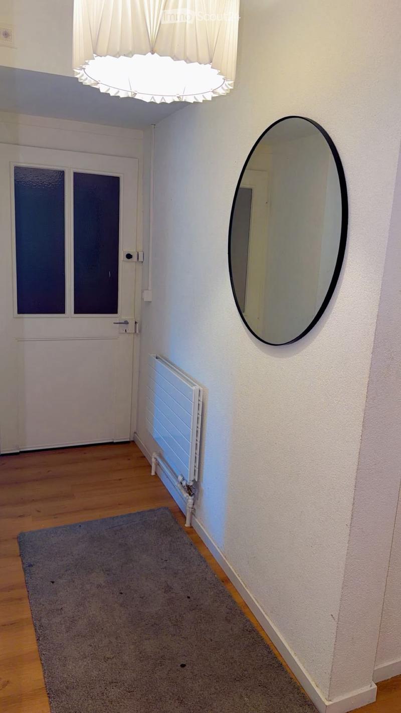 Empty hallway with wooden flooring, white walls, a large round mirror, a radiator, and a door with frosted glass panels.