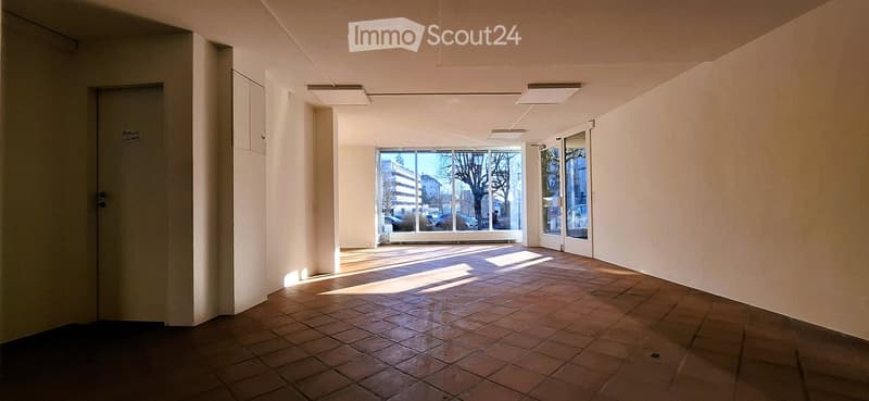 Empty hallway with white walls, brown tile floor, glass windows, recessed ceiling lights, cabinets on the left