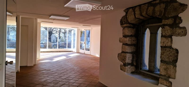Empty room with red tile floor, high ceiling with windows, stone wall with a window