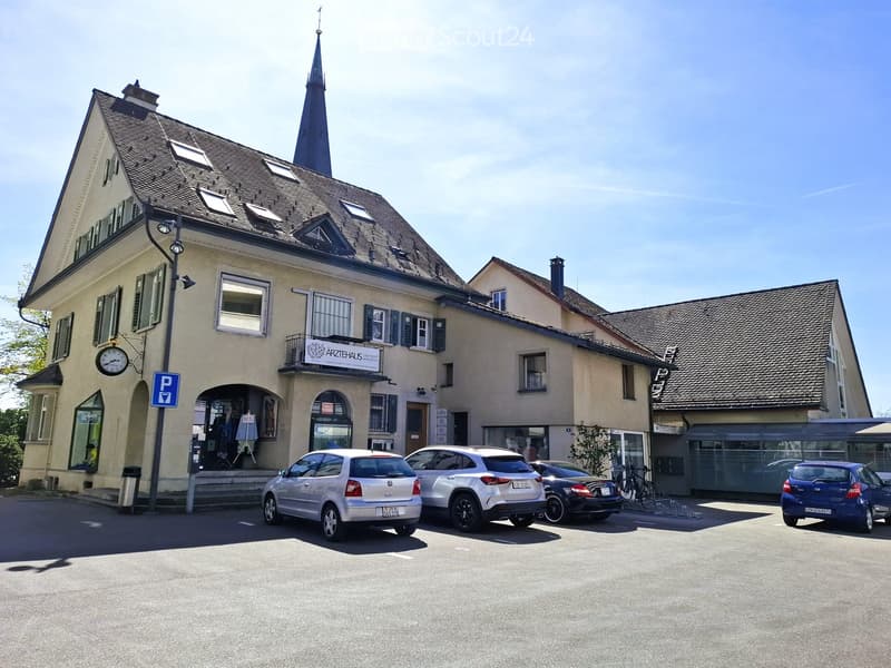 exterior of a building, beige house with a spire on top, multiple cars parked in front, bike stands outside